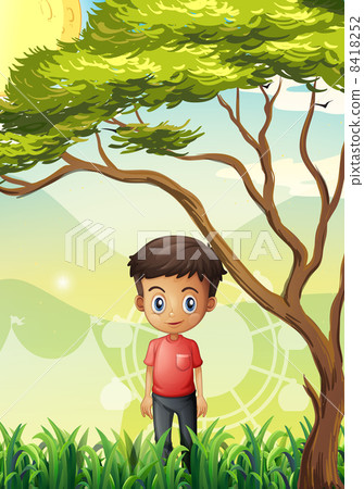 A young man standing at the field near the giant tree 8418252