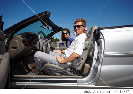Young couple in dark sunglasses sits in cabriolet and looks thr 8431875