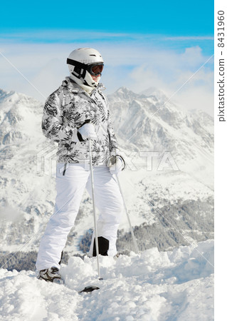 Young woman in ski suit stands on background of mountains and bl 8431960