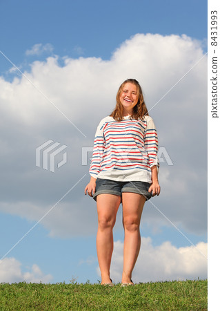Young fat girl in shorts stands at green grass and laughs at bac 8431993