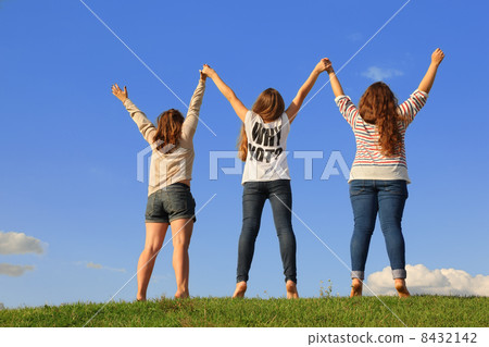 Back of three girls holding hands at green grass at background o 8432142