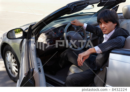 Man in a striped suit sits on a driver seat in a open top car 8432224
