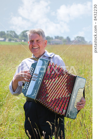 Smile grandfather plays on accordion in field near village 8432230