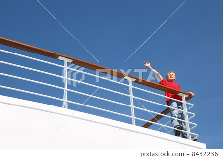 Boy stands at railing on deck of ship, shouts and waves his hand Boy stands at railing on deck of ship, shouts and waves his hand 8432236