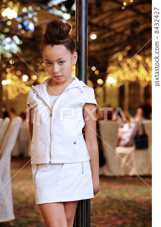 Girl in white leather suit stands near decorative lamppost at ba Girl in white leather suit stands near decorative lamppost at ba 8432427