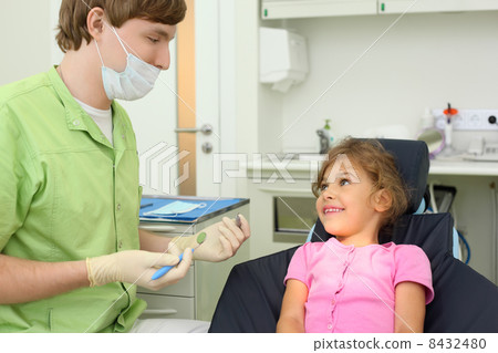 Dentist prepares to treat teeth of girl in dental clinic. Focus 8432480