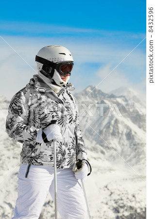 Young woman in ski suit and in helmet stands on background of mo 8432596