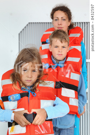 Mother, son and daughter test their orange life jackets at deck 8432597