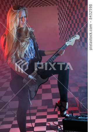 Beautiful girl holds electric guitar in studio in smoke and red 8432598