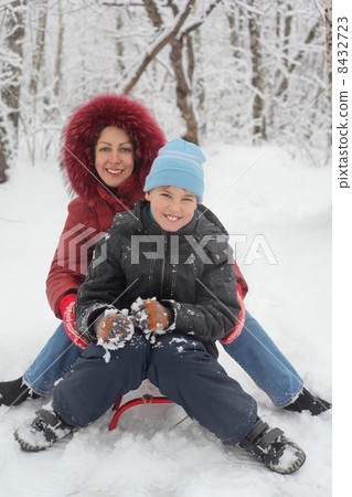 Mother, son ride on sled in winter forest, focus on child 8432723
