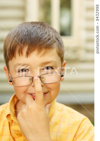 Little boy corrects glasses near wooden village house 8432998