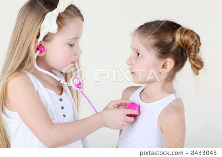 Little girl in white listens heartbeat of another frightened gir Little girl in white listens heartbeat of another frightened gir 8433043