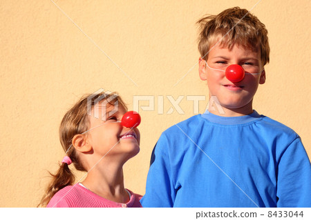 Brother and sister with red clown noses stand near wall and smil 8433044