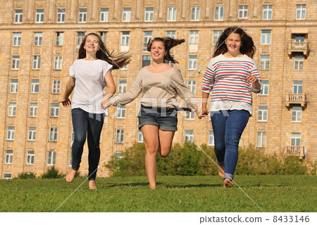 Three smiling girls run at green grass at background of multi-st Three smiling girls run at green grass at background of multi-st 8433146