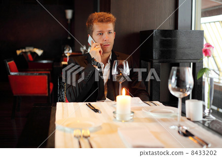Serious young man in a black suit at a restaurant talking on the Serious young man in a black suit at a restaurant talking on the 8433202