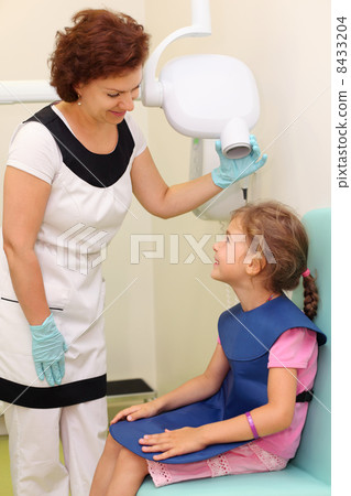Dentist prepares smiling girl wearing in protective lead apron t Dentist prepares smiling girl wearing in protective lead apron t 8433204