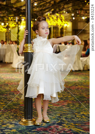 Little girl-model performs white gown, standing near decorative Little girl-model performs white gown, standing near decorative 8433224
