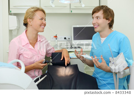 Two smiling dentists sits in cabinet of dental clinic and look a 8433348