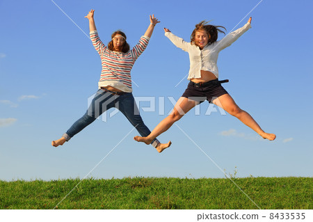 Two young fat girls jump at green grass at background of blue sk 8433535