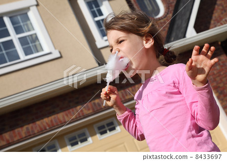 Happy little girl eats cotton candy and looks into distance near Happy little girl eats cotton candy and looks into distance near 8433697