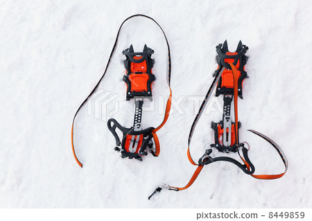 Pair of orange crampons with spikes for mountaineering is on whi 8449859