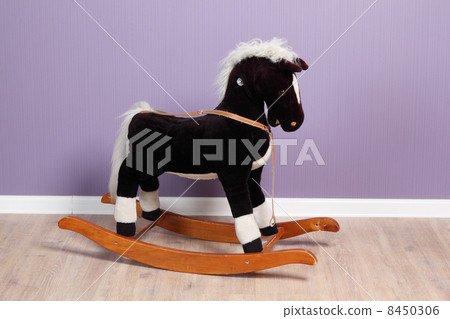 Small rocking horse in room with purple wallpapers 8450306