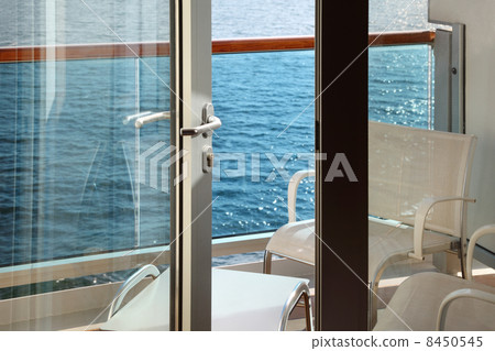 open door; glassy balcony with white chairs and table on cruise open door; glassy balcony with white chairs and table on cruise 8450545