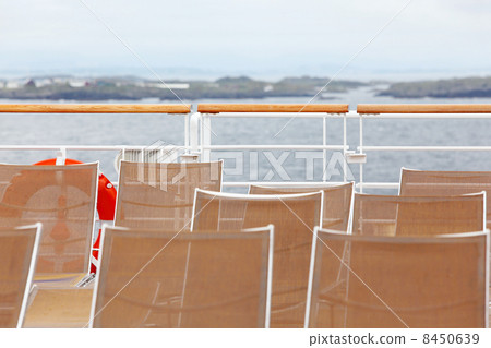 Many sun loungers are on deck of ship. Seashore is seen in dista 8450639