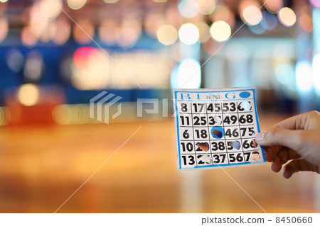 Woman hand holds bingo card with holes at background of big boar Woman hand holds bingo card with holes at background of big boar 8450660