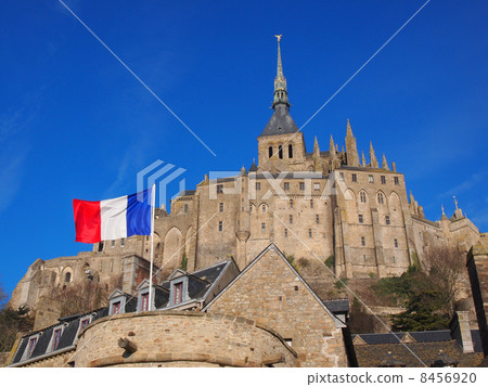 Mont-Saint-Michel rising in the blue sky and the French flag 8456920