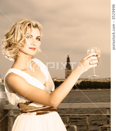 Beautiful blond girl drinks champagne near the river at sunset t 8529996