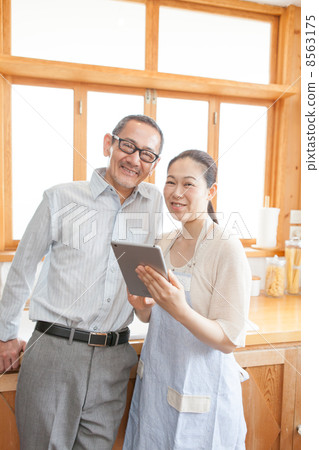 A mature couple looking at a tablet PC in the kitchen A mature couple looking at a tablet PC in the kitchen 8563175