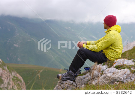 Man Hiker in Mountains relaxing sitting on rocky cliff with clouds on background Man Hiker in Mountains relaxing sitting on rocky cliff with clouds on background 8582642