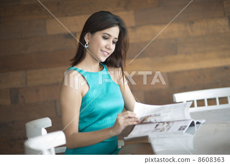 Woman seated on chair reading magazine on table Woman seated on chair reading magazine on table 8608363