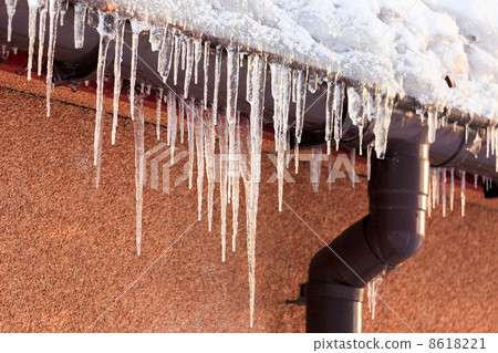 Winter icicles hanging from eaves of roof 8618221