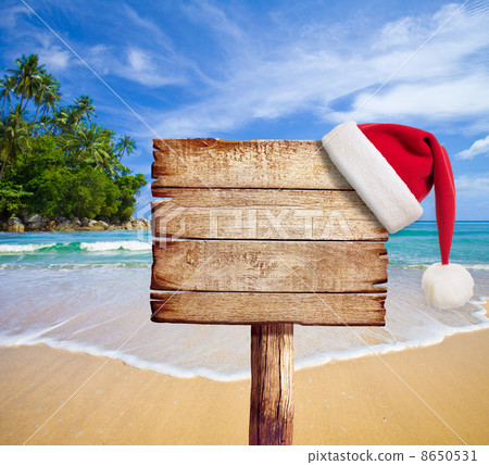 Christmas on beach. Wooden signboard with Santa's hat. 8650531