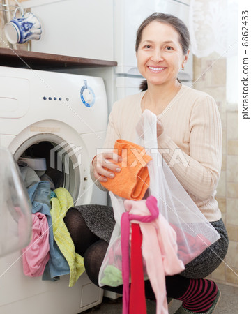 mature housewife loading the washing machine mature housewife loading the washing machine 8862433
