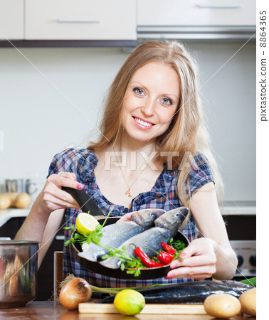 Smiling blonde woman cooking lubina in frying pan Smiling blonde woman cooking lubina in frying pan 8864365