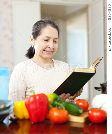 woman reads cookbook for recipe in kitchen 8864880