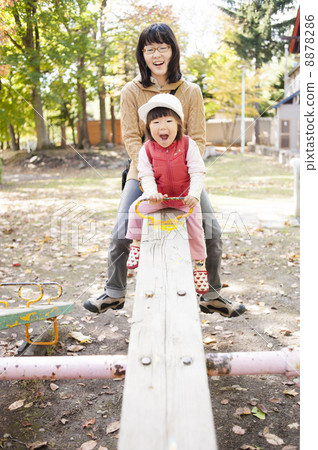 Parent and child playing with a seesaw Parent and child playing with a seesaw 8878286