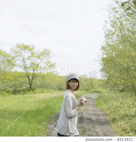 A woman holding a mirror-less single-lens camera and looking back at one road A woman holding a mirror-less single-lens camera and looking back at one road 8913931