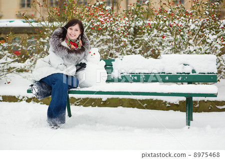Girl sitting on the bench with funny snowman Girl sitting on the bench with funny snowman 8975468