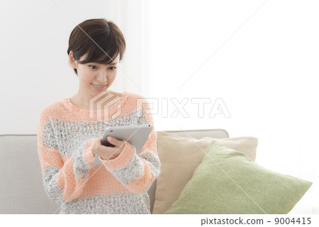 A woman sitting on a sofa to search the net with a tablet 9004415