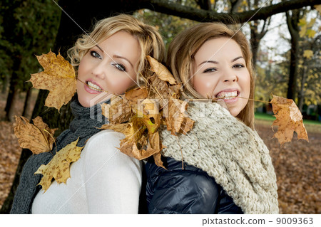 Two beautiful women with dry leaves in the teeth by autumn. 9009363