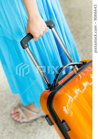 Woman in blue dress holds orange suitcase in hand 9066643