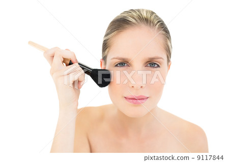 Frowning fresh blonde woman applying powder on her cheeks Frowning fresh blonde woman applying powder on her cheeks 9117844