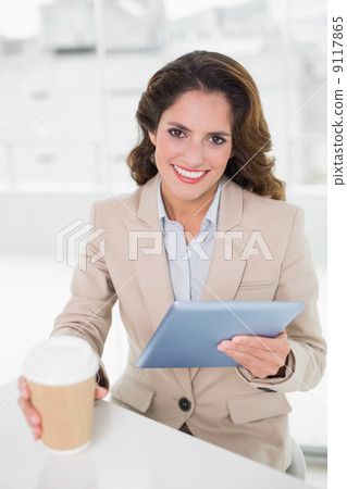 Smiling businesswoman using digital tablet at her desk holding d Smiling businesswoman using digital tablet at her desk holding d 9117865