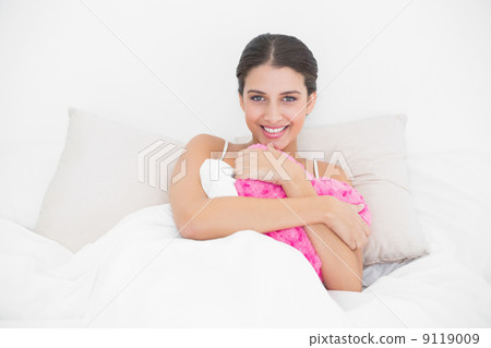 Happy young brown haired model in white pajamas hugging a heart 9119009