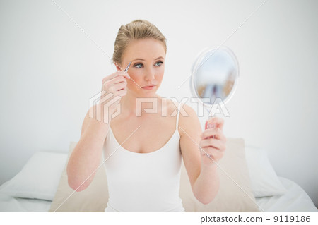Natural serious blonde holding mirror and using tweezers 9119186