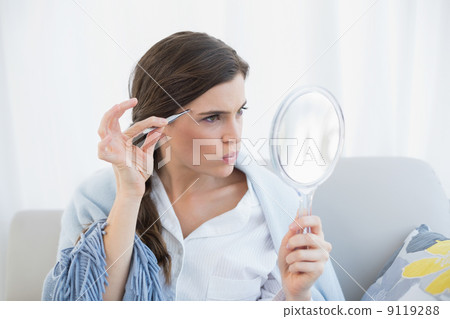 Focused casual brown haired woman in white pajamas plucking her Focused casual brown haired woman in white pajamas plucking her 9119288